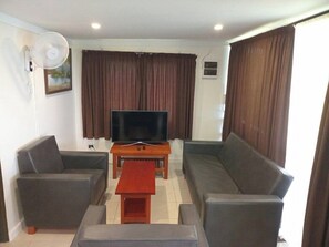 A living room with a flat-screen TV, a sofa, a coffee table, and a fan. - Dreamview Villas (Rakiraki)