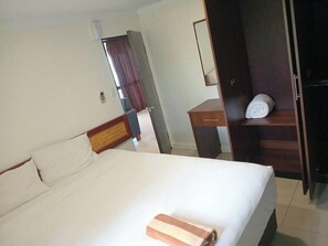 A hotel room with a bed, a wooden headboard, a desk, a wardrobe, and a bathroom door. - Dreamview Villas (Rakiraki)