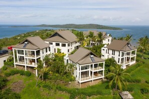 A coastal property with multiple white buildings featuring large windows and balconies, surrounded by lush greenery and a view of the ocean. - Dreamview Villas (Rakiraki)