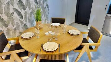 Een ronde houten eettafel, gedekt met borden, glazen en bestek, omringd door stoelen met donkere kussens.