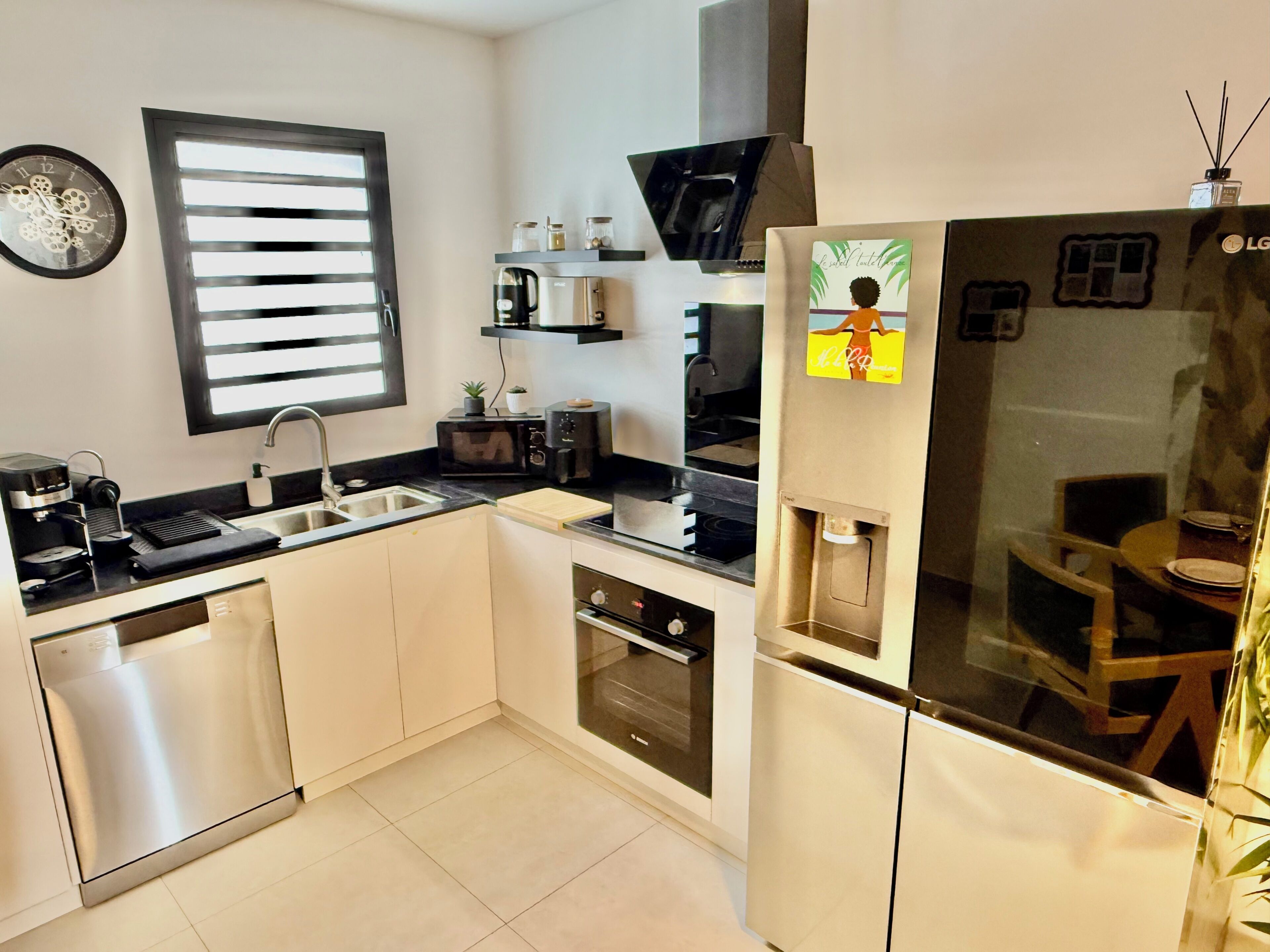 Een moderne keuken met een vaatwasser, spoelbak, magnetron en een koelkast met waterdispenser.