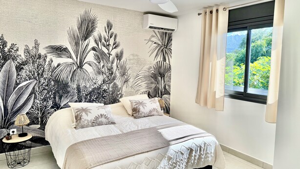 Quarto com cama, ventilador de teto, ar condicionado, janela com cortinas e parede com estampa botânica.