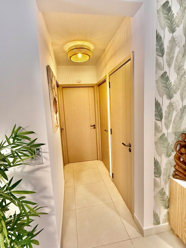 A hallway with a wooden door, a wall-mounted light fixture, and a potted plant.