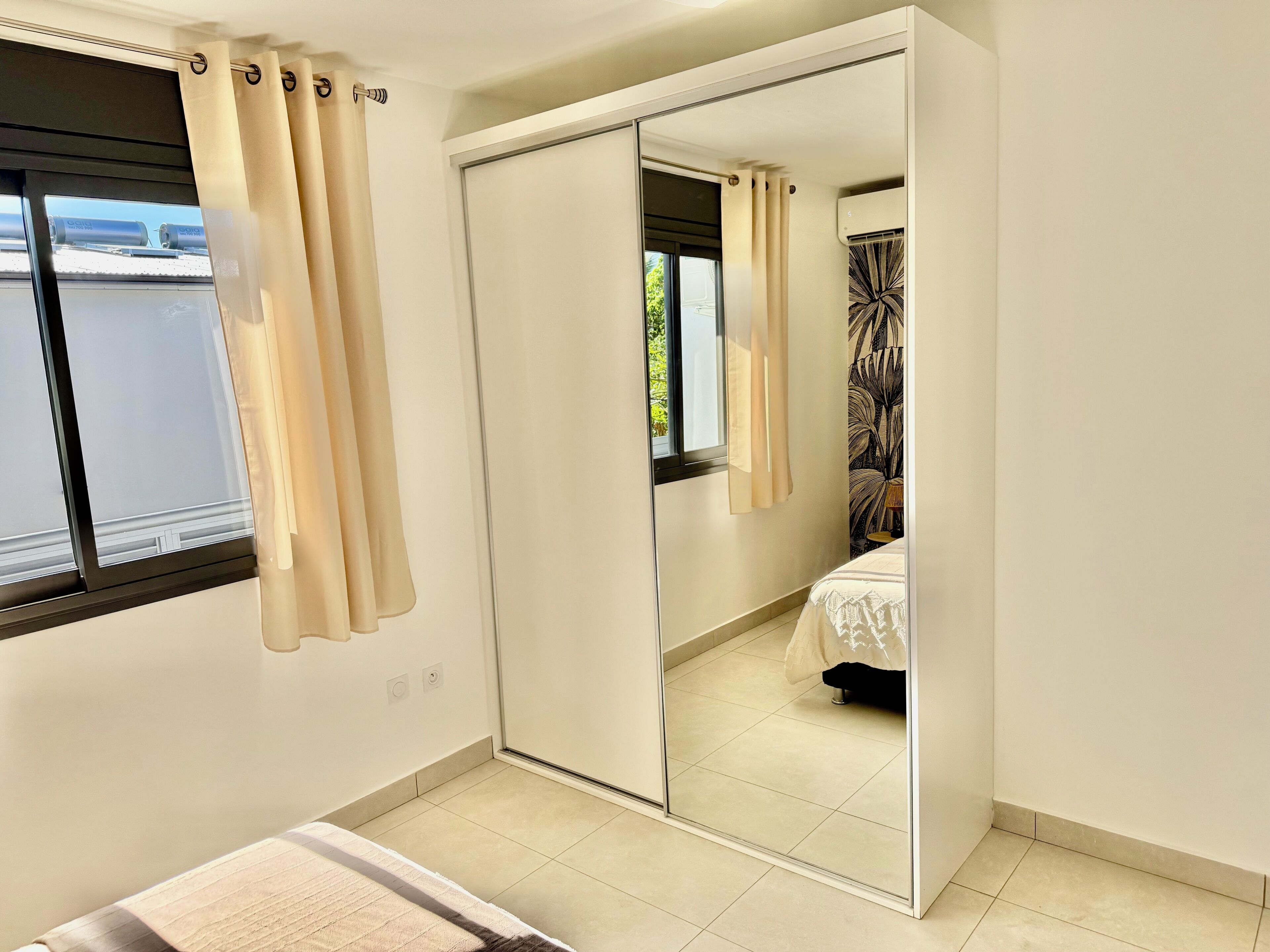 Een slaapkamer met een schuifdeurkast, een bed met een witte spreideken, en een raam met gordijnen.