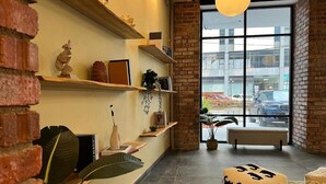A cozy interior with brick walls, shelves with decorative items, a large window with a view of the street, and a bench. - Swing & Pillows @ CIQ Johor Bahru (Johor Bahru)