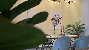 A dining area with a table, chairs, a vase with flowers, and a wall-mounted light fixture. - Swing & Pillows @ CIQ Johor Bahru (Johor Bahru)