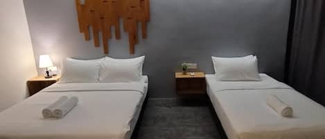 A hotel room with two beds, a wall-mounted light fixture, and a small bedside table with a lamp.