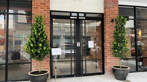 A building entrance with glass doors, potted plants, and a brick wall. - Swing & Pillows @ CIQ Johor Bahru (Johor Bahru)