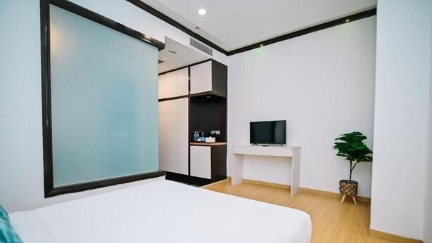 Una habitación de hotel moderna con una cama, televisión, escritorio pequeño y planta.