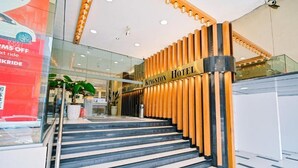Entrada de un hotel con una escalera que lleva a la recepción, destacando un diseño de paneles de madera y un letrero que dice 'Kingston Hotel'.