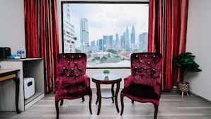 Una habitación con dos sillas, una mesita y una planta. Se ve una vista panorámica de la ciudad por la ventana.
