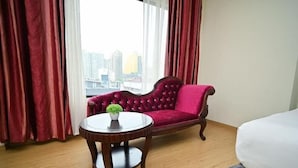 Una habitación de hotel con un sofá de terciopelo rojo, una mesa redonda de madera con una planta en maceta y una cama.