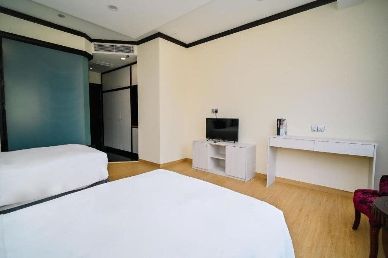Ein Hotelzimmer mit zwei Betten, einem Schreibtisch, einem Fernseher und einem Kleiderschrank.