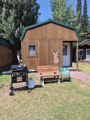 A wooden cabin with a porch, a bench, a grill, and a deer head decoration. - 2 bedroom Family room with ensuite bathroom (Essex)