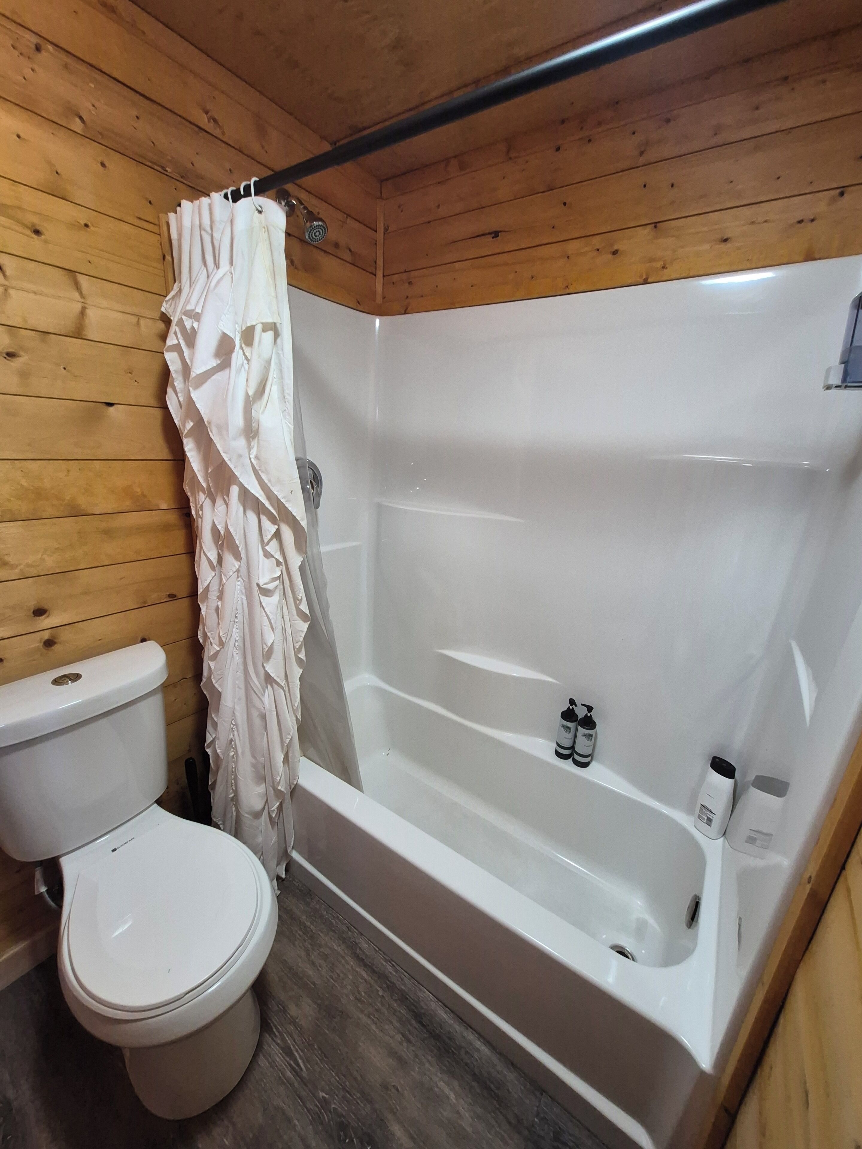 A bathroom with a white bathtub, a toilet, and a shower curtain.