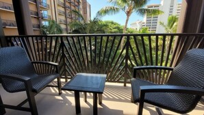 A balcony with two chairs and a small table, surrounded by a wooden railing, overlooking a residential area with palm trees and buildings. - Ko Olina | Couples Disney Retreat | Lagoon + Pool (Kapolei)