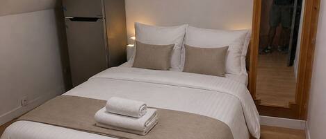 A bedroom with a bed, a refrigerator, and a wooden door.