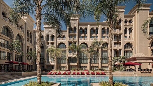 A hotel with a large pool, palm trees, and red lounge chairs. - Giza Palace (Sheikh Zayed City)