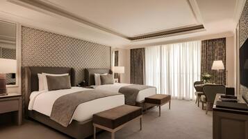 A hotel room with two beds, a desk, a chair, and a TV.