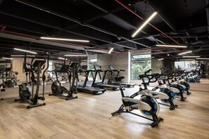 Ein Fitnessstudio mit unterschiedlichen Trainingsgeräten, darunter Laufbändern und Ergometer, sowie einem Holzboden.