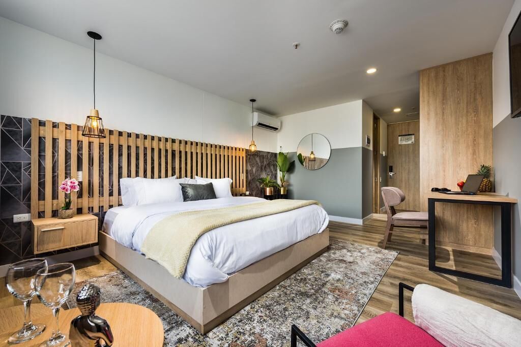 Quarto moderno com cama, mesas de cabeceira, espelho, escrivaninha e cadeira.