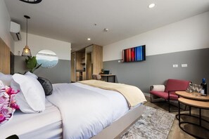 Ein modernes Hotelzimmer mit einem Bett, einer Sitzecke mit Tisch und einem an der Wand befestigten Fernseher.