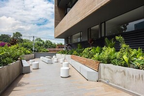 Eine Dachterrasse mit Sitzgelegenheiten im Freien, Pflanzen und einer modernen Gebäudefassade.
