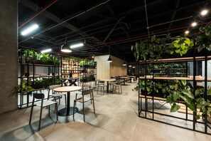 Un espace intérieur aménagé avec des tables et des chaises, des étagères ornées de plantes et des plantes suspendues.