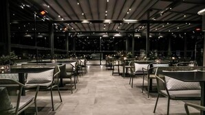 An indoor dining area with tables and chairs arranged in rows, large windows along one side, and a ceiling with recessed lighting. - Liberty (Nafplio)