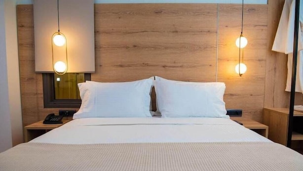A hotel room with a wooden headboard, a bed with white bedding, and two bedside lamps. - Liberty (Nafplio)