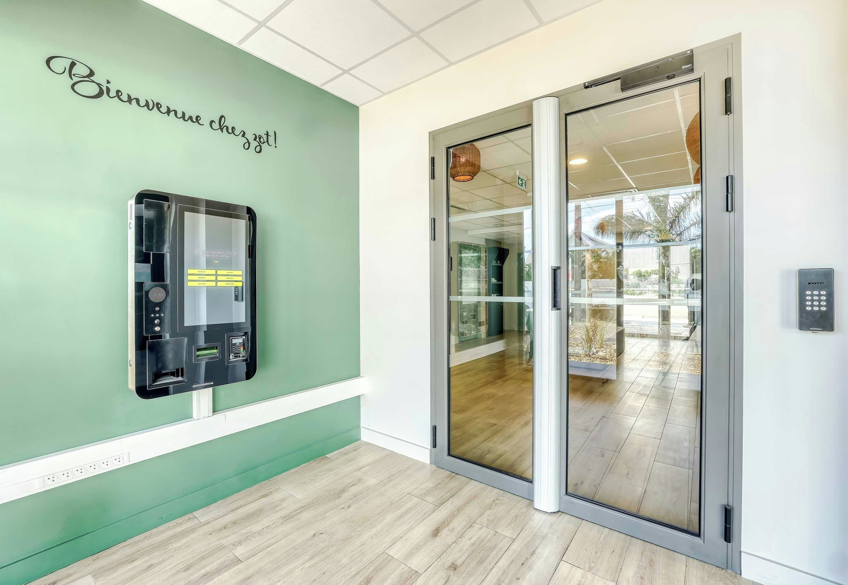 Een hotel receptie met een groene wand, een receptiebalie en een glazen deur naar een balkon.