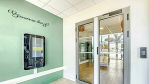 Zona de recepción de un hotel con una pared verde, un mostrador de recepción y una puerta de cristal que da a un balcón.