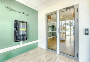 A hotel reception area with a green wall, a reception desk, and a glass door leading to a balcony.