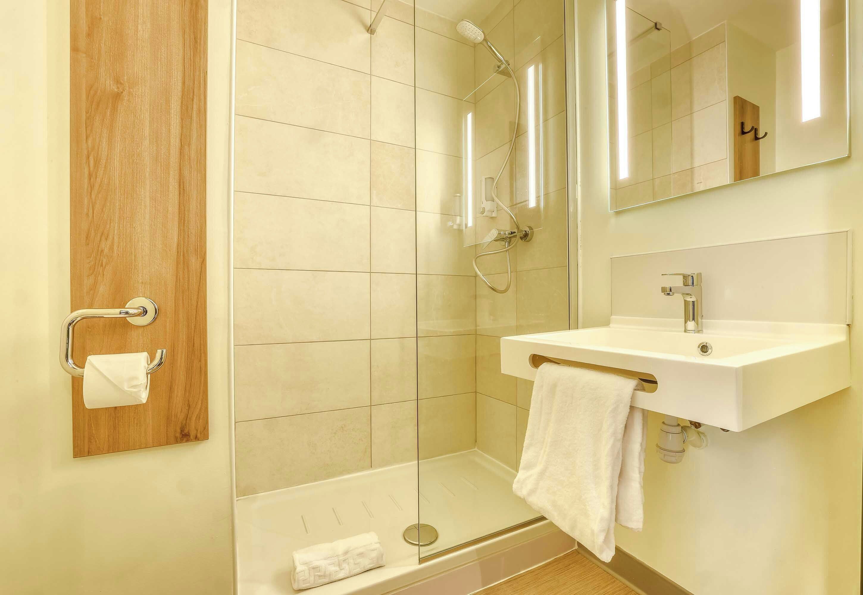 A modern bathroom with a glass shower enclosure, a wooden panel, a white sink, and a mirror.