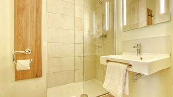 A modern bathroom with a glass shower enclosure, a wooden panel, a white sink, and a mirror.