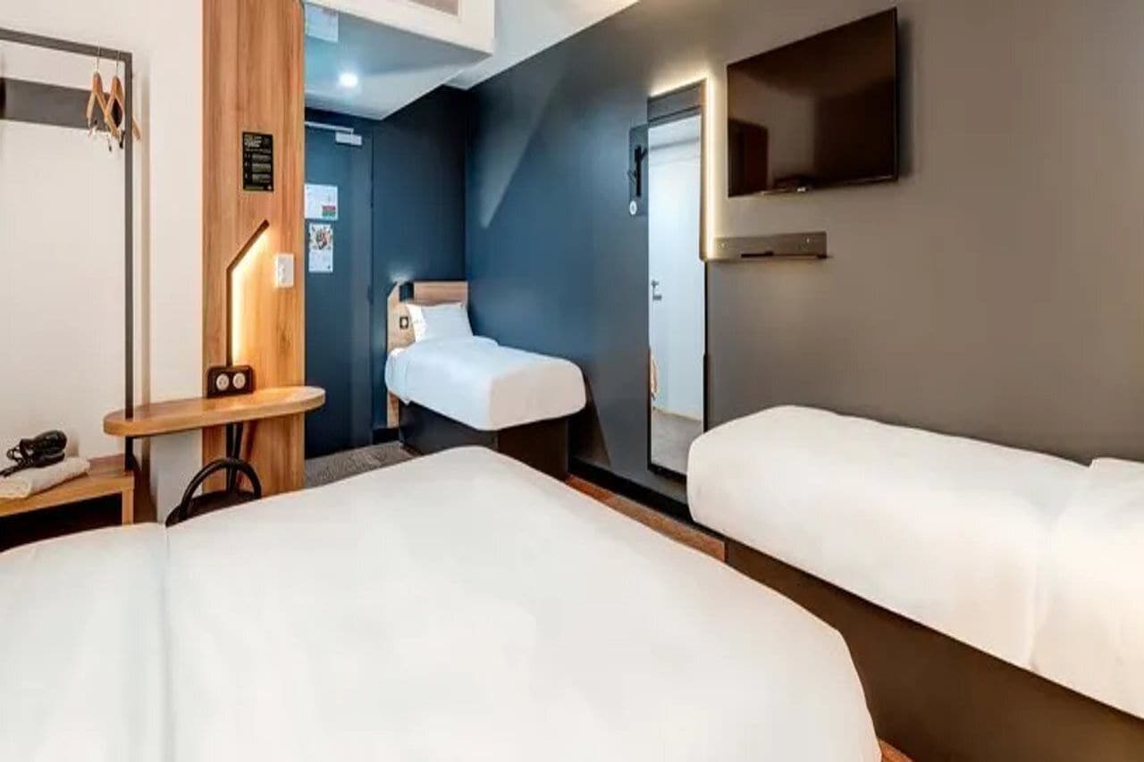 Ein Hotelzimmer mit zwei Betten, einem Schreibtisch, einem Stuhl, einem Fernseher und einem Spiegel.