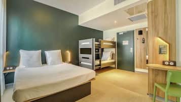 A hotel room with a bed, a desk, and a chair. There is a wardrobe and a door in the background.