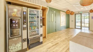 Zona de máquinas expendedoras con bebidas y aperitivos, piso de madera y una puerta con pared verde.