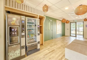 A vending machine area with a selection of beverages and snacks, a wooden floor, and a door with a green wall.