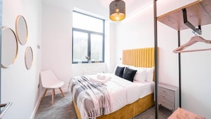 A bedroom with a bed, a chair, a window, a hanging light fixture, and a wardrobe. - Snoozeden Wellesley - Near to Slough Station (Cardiff)
