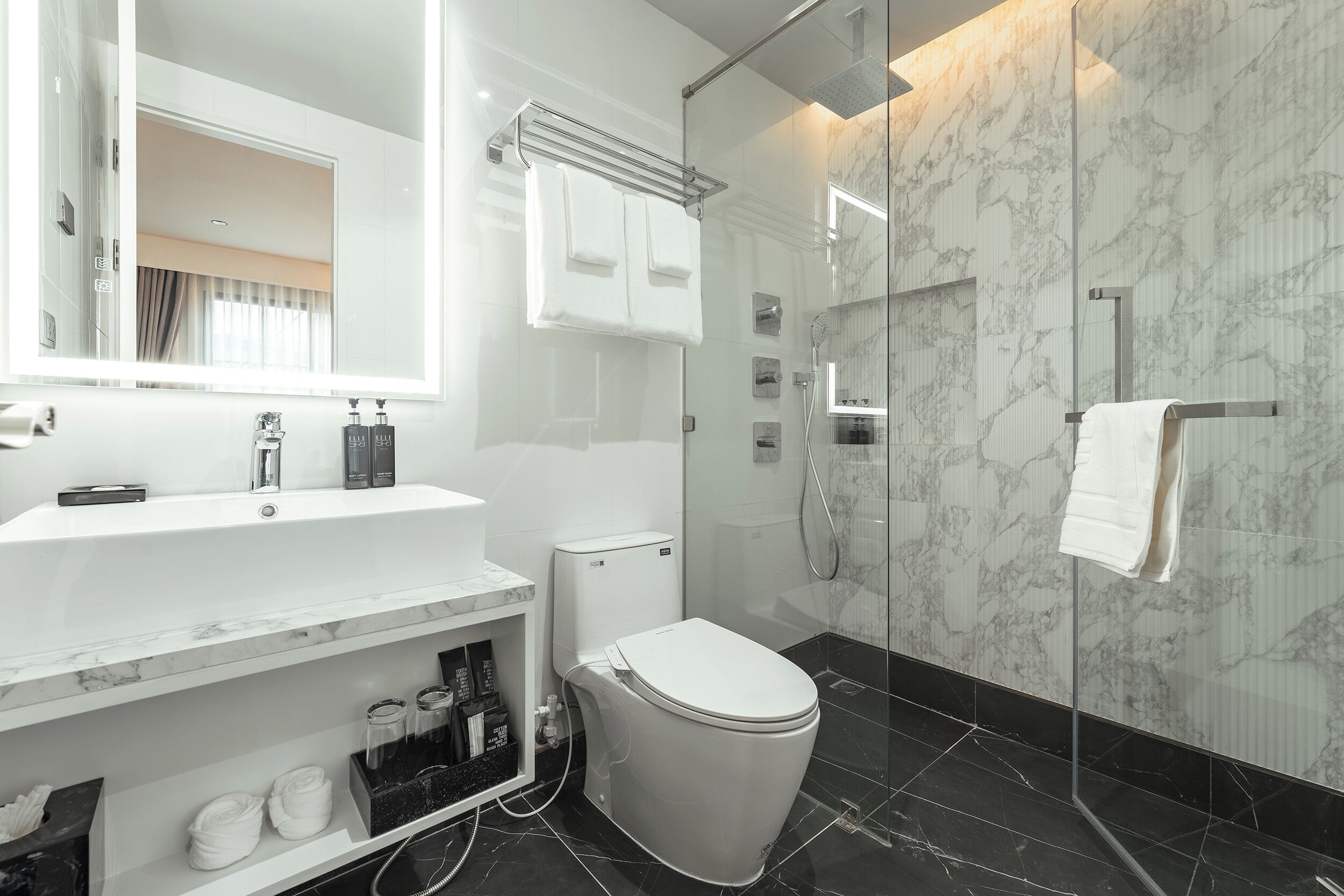 A modern bathroom with a marble sink, a toilet, and a glass-enclosed shower area.