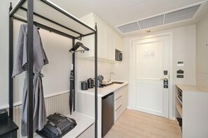 A compact hotel room with a kitchenette, a built-in wardrobe, and a door with a security lock. - Chateau Du Village Patong (Krabi)