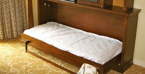 Een eenpersoonsbed met houten frame en witte beddengoed in een kamer met een kamerbreed tapijt en een gordijn met stippen.
