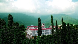 A hotel with multiple buildings, surrounded by dense greenery and mountains in the background. - The Vaishno Devi Sarovar Portico Katra (Reasi)