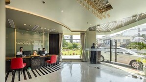 A hotel reception area with a modern design, featuring a reception desk, red chairs, and a view of the street outside. - The Vaishno Devi Sarovar Portico Katra (Reasi)