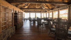 Un'area pranzo all'aperto coperta, con tavoli e sedie in legno, un tetto di paglia e vista sul paesaggio circostante.