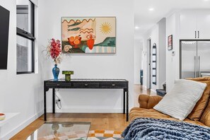 Una sala de estar moderna con sofá, mesa de centro, un cuadro y una cocina con refrigerador.
