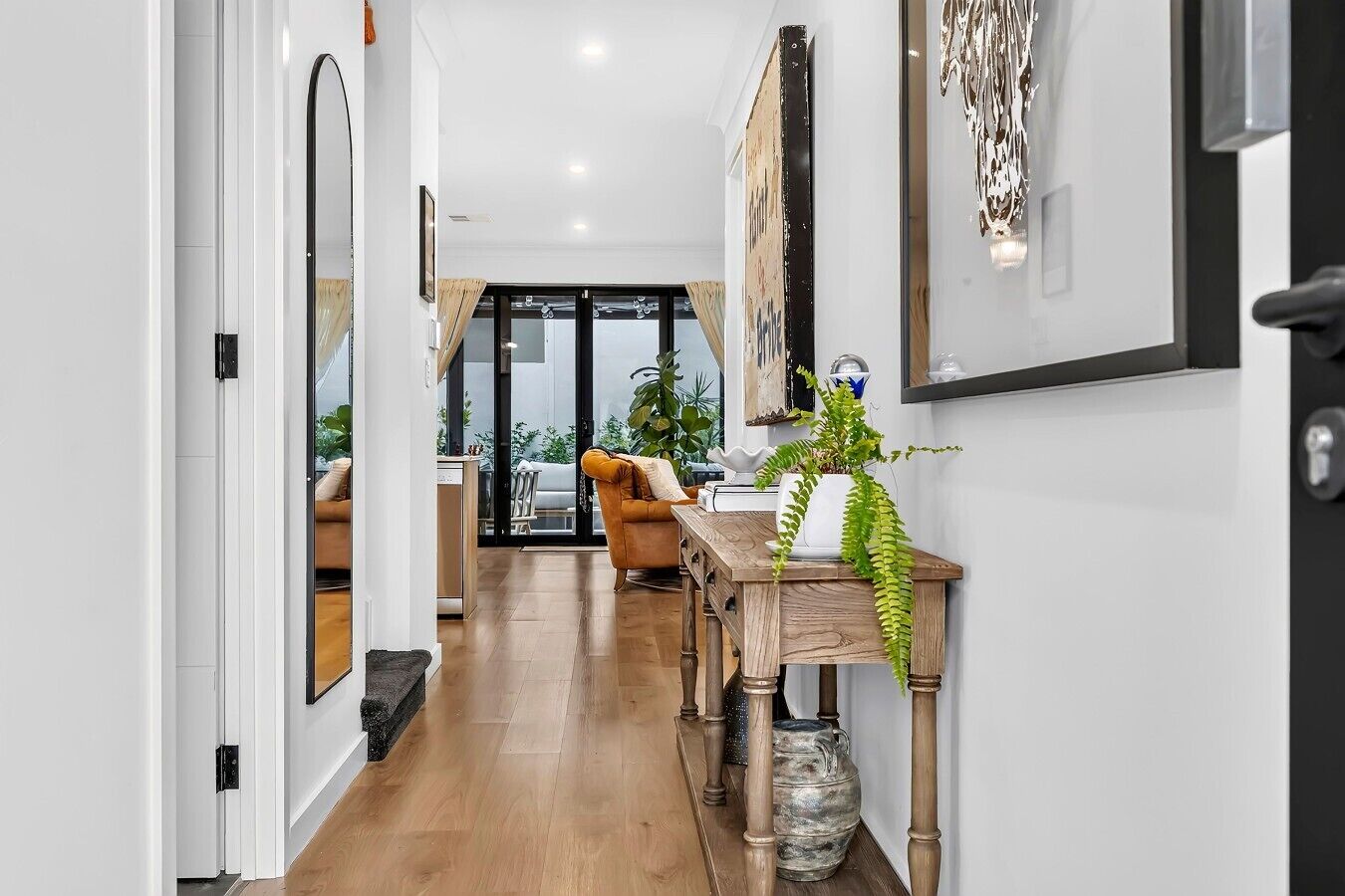 A hallway with a wooden floor, a sofa, a dining table, and a plant.