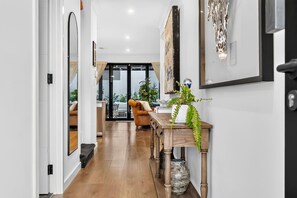 A hallway with a wooden floor, a sofa, a dining table, and a plant. - The Art House | Courtyard + Alfresco Living (Campbelltown)