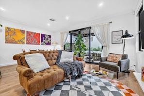 Un salon moderne avec un canapé en cuir marron, un canapé gris, un tapis à carreaux et une grande fenêtre avec des rideaux.